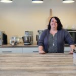 Katrin Schulz in ihrer Backstube hinter einm großen Holztisch und vor verschiedenen Geräten zur Brotzubereitung